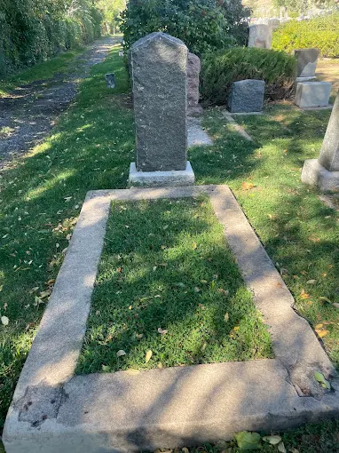 Close view of a historic upright headstone and grave border beside a shaded path at Golden Hill Cemetery