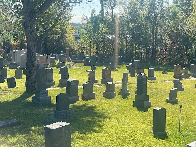 Shaded headstones beneath a mature tree on the well-kept grounds of Golden Hill Cemetery